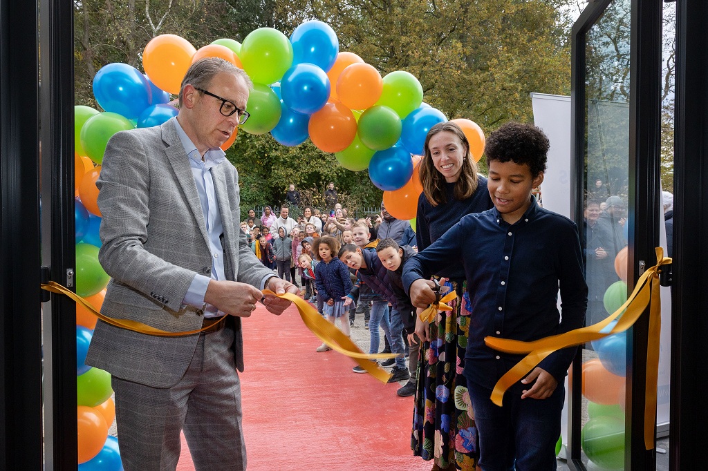Wethouder Dennis Grimbergen en een leerling knippen samen een lint door bij de heropening van de Timotheüsschool