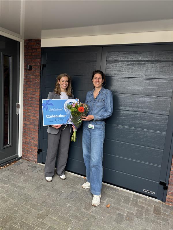Winnaar van de eindejaarsverloting van het LelystadPanel 2025, Karin Uffels ontvangt van Martiene van het Datateam een Cadeaubon ter waarde van 250 euro.