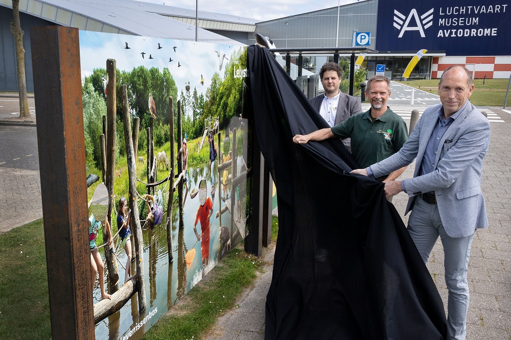 Aviodrome-directeur Roy Imker, voorzitter Andre Rijsdorp van het Belevenissenbos en wethouder Piet van Dijk onthullen het informatiebord bij het Aviodrome