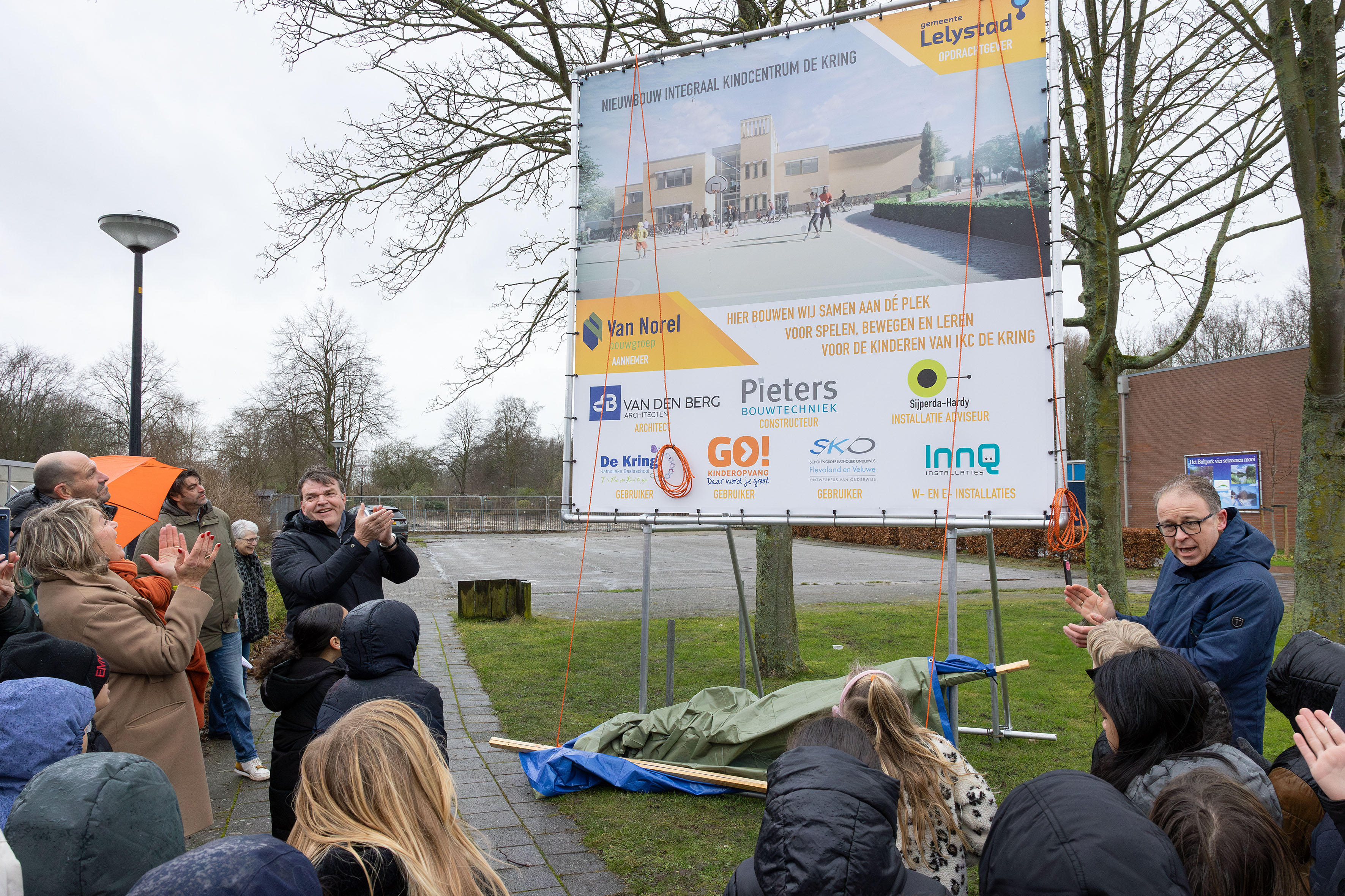 Wethouder Dennis Grimbergen en andere mensen staan bij een bord waarop het nieuwe kindcentrum te zien is 
