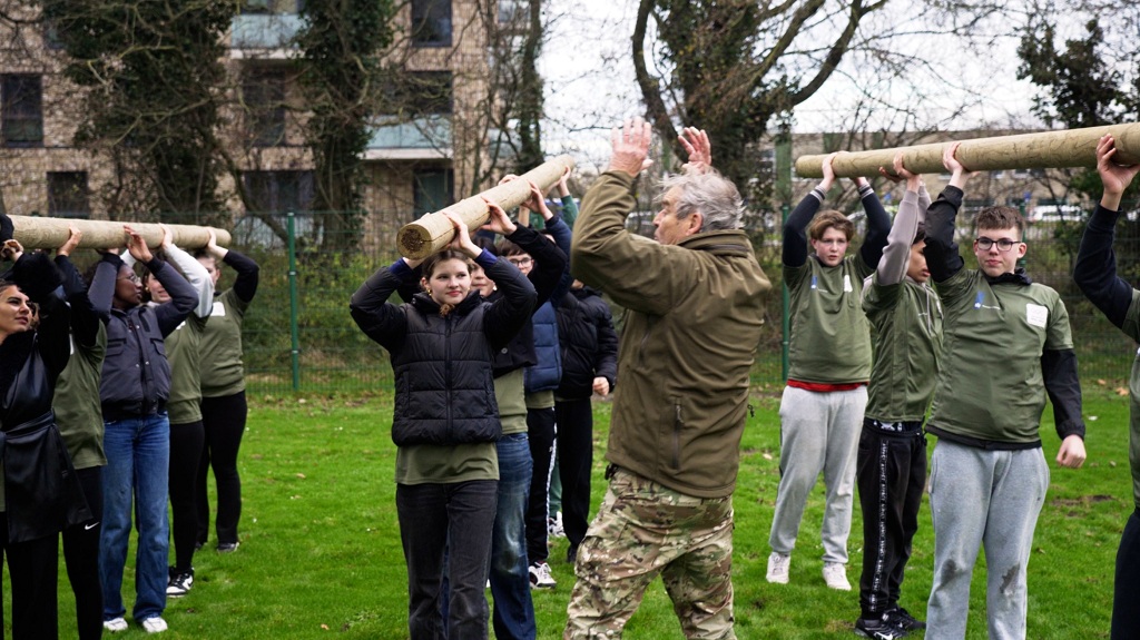 Leerlingen van Porteum houden in teamverband boomstammen boven hun hoofd (Foto: Jarno de Groot)